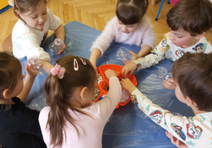 Dzieci wykonują serca - wrzucają pompony, brokat, błękitne i białe cekiny