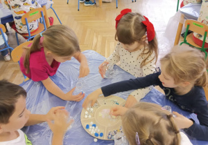 Dzieci wykonują serca - wrzucają pompony, brokat, błękitne i białe cekiny