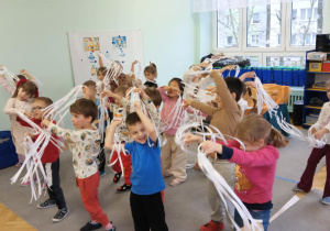 Dzieci tańczą do muzyki z Królowej Śniegu, w ręku trzymając białe wstążki