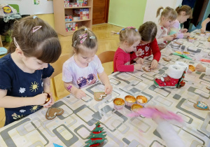 dzieci siedzą przy stole i ozdabiają pierniki