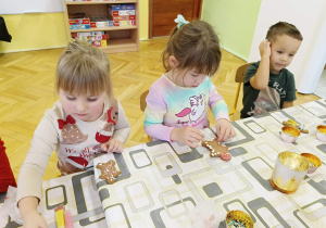 dzieci siedzą przy stole i ozdabiają pierniki