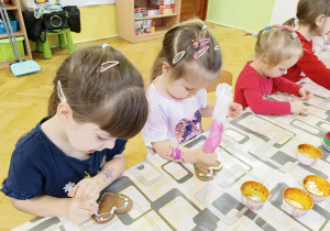 dzieci siedzą przy stole i ozdabiają pierniki