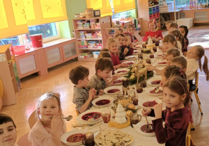 dzieci wspólnie siedzą przy świątecznym stole, spożywają potrawy