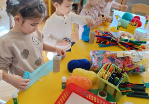 dzieci siedzą przy stolikach, wykonują kukiełki
