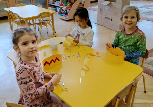 dzieci siedzą przy stolikach, wykonują korony