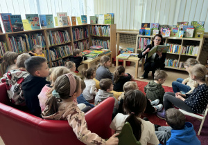 Dzieci siedzą na dywanie i słuchają pani czytającej książkę
