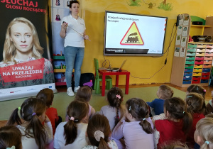 dzieci siedzą na dywanie, zapoznają się ze znakami drogowymi znajdującymi się przy przejazdach kolejowych