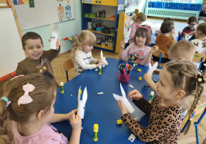 Dzieci siedzą przy stolikach, przy pomocy artykułów papierniczych wykonują króliczka wielkanocnego.