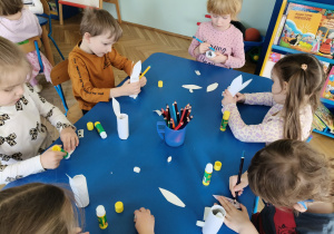 Dzieci siedzą przy stolikach, przy pomocy artykułów papierniczych wykonują króliczka wielkanocnego.