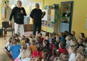 Panowie przedstawiają instrumenty dzieciom siedzącym na dywanie