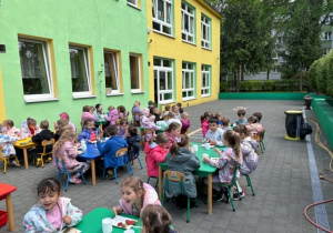 dzieci siedzą przy stolikach na tarasie spożywając posiłek