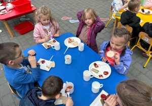 dzieci siedzą przy stolikach na tarasie spożywając posiłek