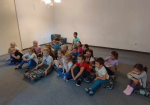 Dzieci z grupy zielonej siedzą na poduszkach na dywanie czekają na teatrzyk Kamiszibai