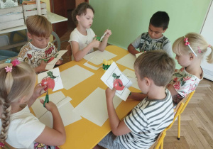Dzieci siedząc przy stoliku wycinają puzzle z ilustracją jabłka.