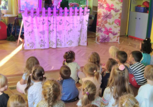 dzieci siedzą na dywanie i oglądają przedstawienie