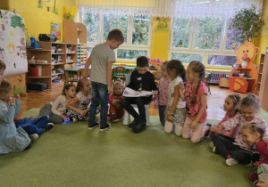 Chłopiec czyta książkę, dzieci siedzą wokół niego