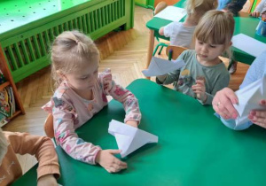 Dzieci składają łódki z białego papieru