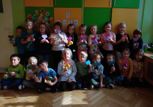 Dzieci pozują do zdjęcia grupowego, trzymając swoje prace