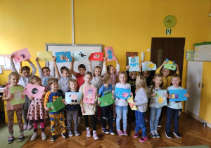 Dzieci pozują do zdjęcia grupowego, trzymając swoje prace