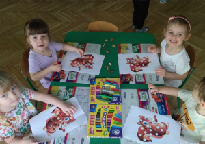Dzieci siedzą przy stoliku, wyklejają brakujące elementy wiewiórki plasteliną