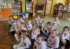 Dzieci siedzą na dywanie, oglądają film o życiu jeży