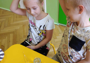 dzieci siedzą przy stołach prowadzą eksperymenty.