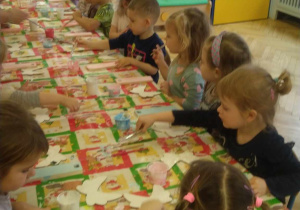 Dzieci siedzą przy stole, wykonują drewniane aniołki