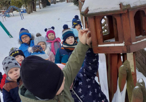 dzieci wsypują ziarno do karmnika dla ptaków