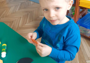dziecko siedzi przy stoliku i z kół origami klei pingwina.