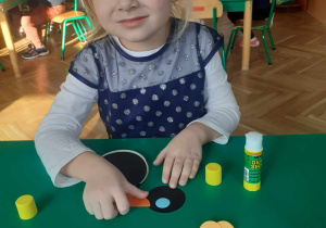 dziecko siedzi przy stoliku i z kół origami klei pingwina.