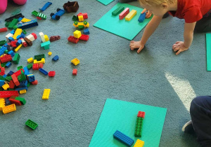 Dzieci siedzą na dywanie i bawią się klockami Lego
