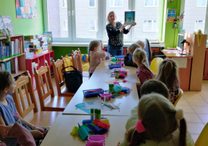 Dzieci siedzą i słuchają czytane książki.