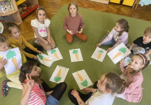 Dzieci siedzą w kole na dywanie - prezentują swoje prace