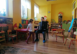 Chłopiec gra na akordeonie, dziewczynka podchodzi do instrumentu