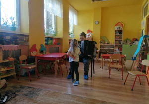 Chłopiec gra na akordeonie, dziewczynka podchodzi do instrumentu