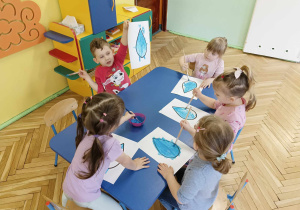 Dzieci siedzą przy stoliku, malują farbami kroplę wody