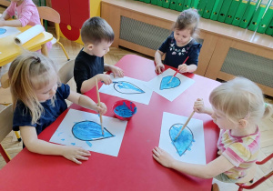 Dzieci siedzą przy stoliku, malują farbami kroplę wody