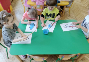 Dzieci siedzą przy stoliku, malują farbami kroplę wody