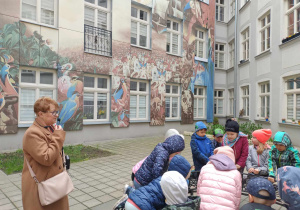 Dzieci podziwiają reprodukcje obrazów Wojciecha Siudmaka z wielkoformatowych płyt gresowych na elewacji kamienicy, obrazy przedstawiają "Baśniowe Światy".