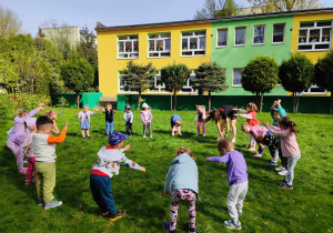 Dzieci wraz z trenerem stoją w kole, wykonują rozgrzewkę przed treningiem karate