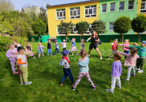 Dzieci stoją w kole, trener prezentuje chwyty karate.