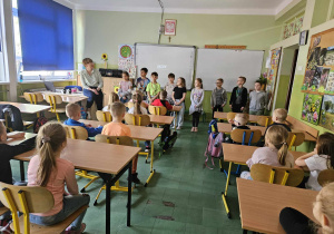 Dzieci siedzą w ławkach, grupa uczniów się przedstawia.