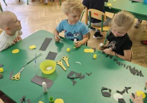 dzieci siedzą przy stoliku, przyklejają elementy pszczoły