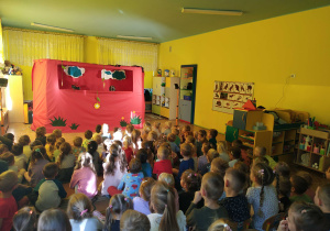 dzieci siedzą na dywanie i krzesłach, oglądają przedstawienie