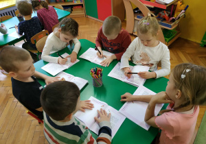 Dzieci siedzą przy stolikach, wykonują ćwiczenia w książkach