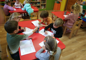 Dzieci siedzą przy stolikach, wykonują ćwiczenia w książkach
