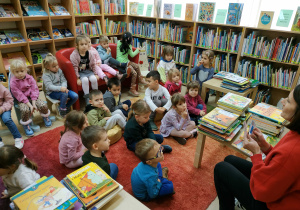 dzieci siedzą na kanapach, krzesłach, pufach, dywanie, słuchają jak można zapisać się do biblioteki
