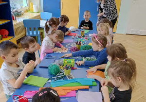 dzieci siedzą przy stolikach, wykonują kartki świąteczne