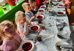 Dzieci siedzą przy stole, spożywają posiłek