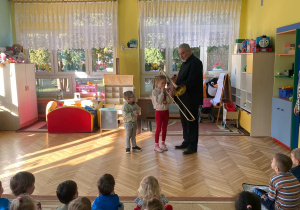 Dwójka dzieci stoi na dywanie i gra na puzonie
